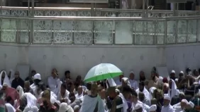 رجل أمن بالمسجد الحرام يحمي معتمراً من حرارة الشمس خلال خطبة أول جمعة برمضان